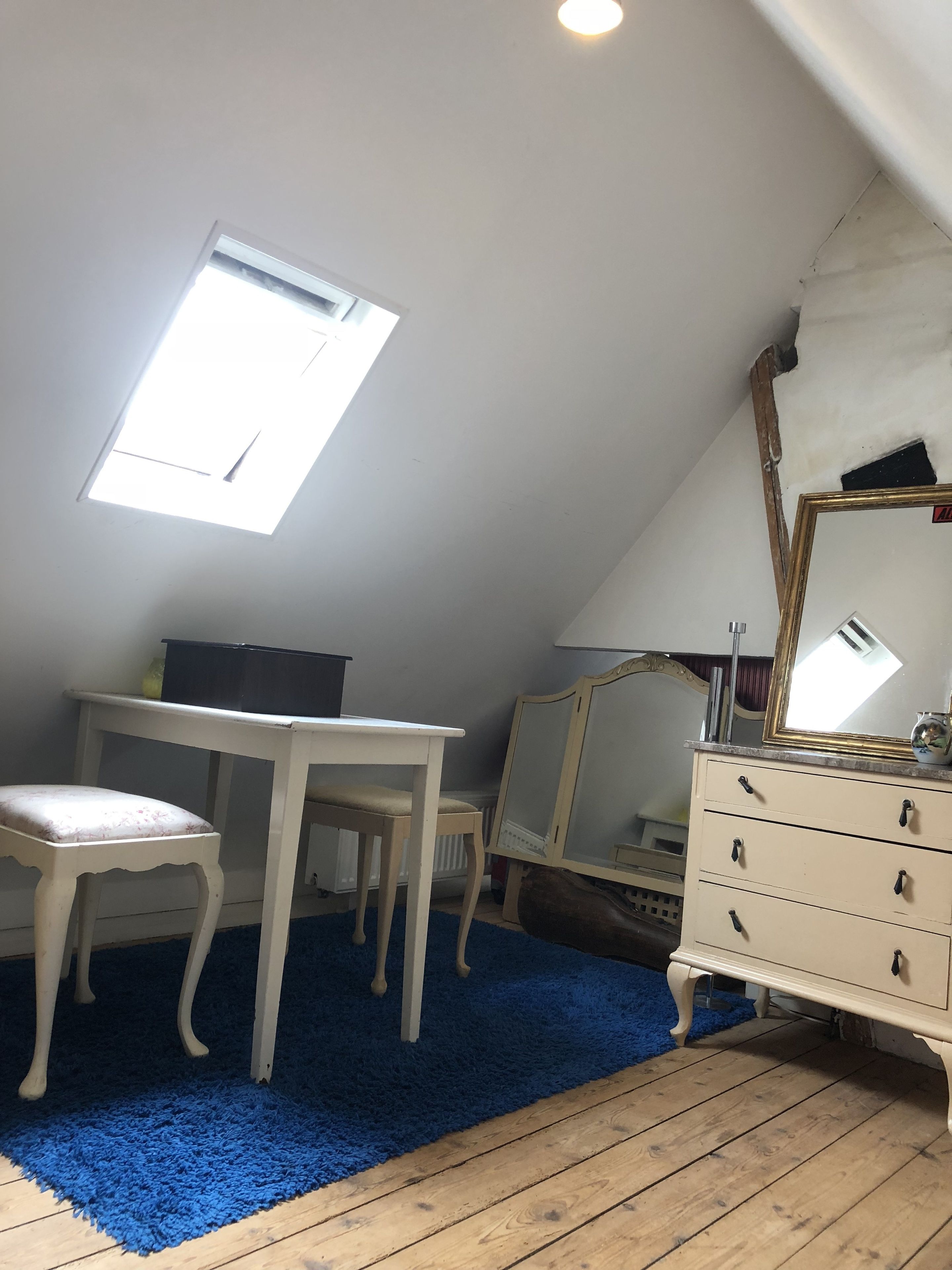 A room with a sloped ceiling, a white desk with a chair, a dresser, and a mirror.