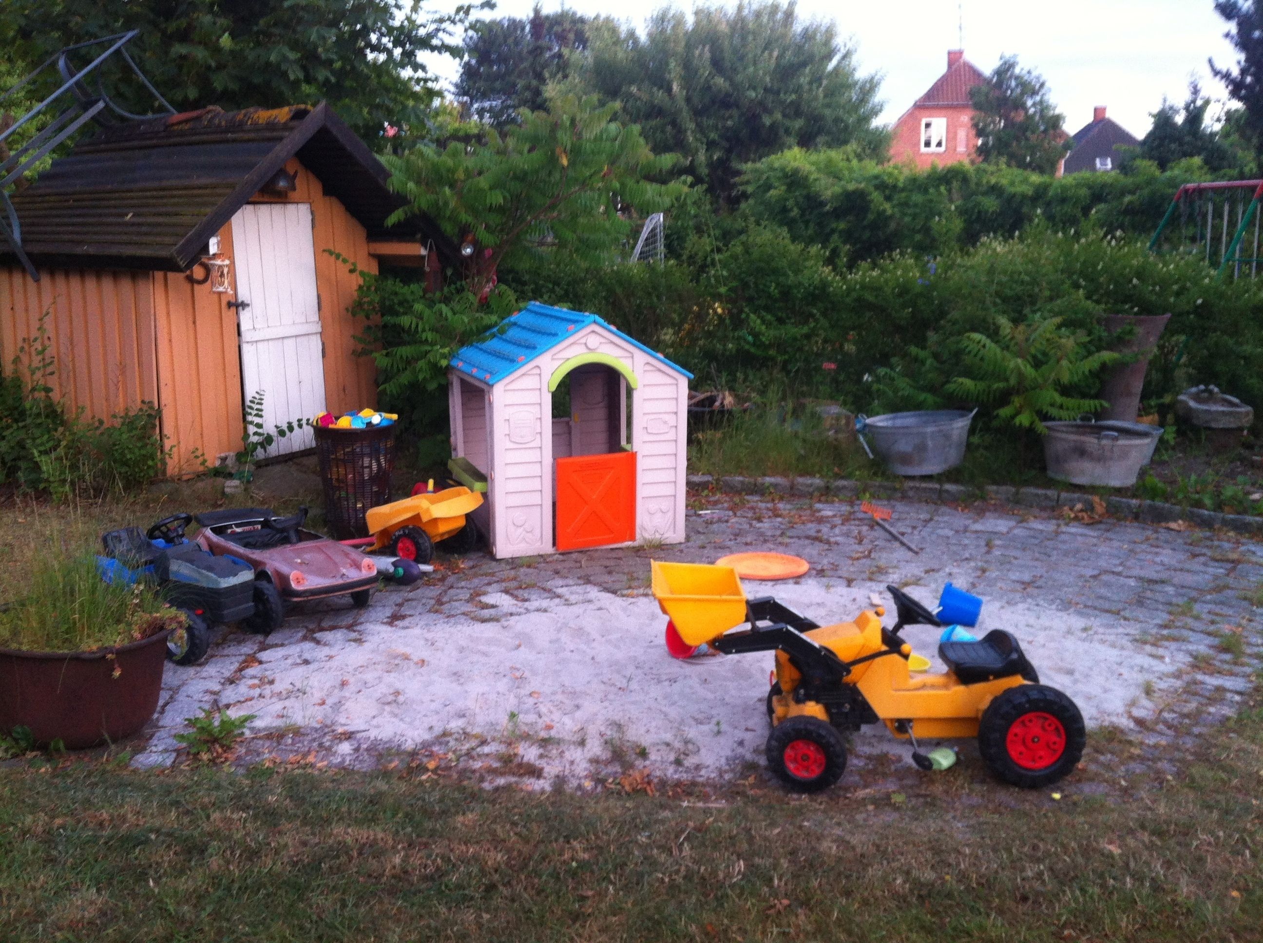 A backyard with a playhouse, a small shed, and various toys.