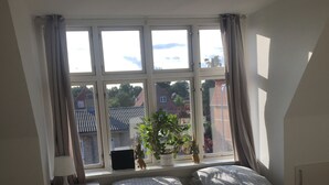 A bedroom with a large bed, a window with curtains, a bedside table with a lamp, and a view of the outside. - Køge Bed & Kitchen (Koge)