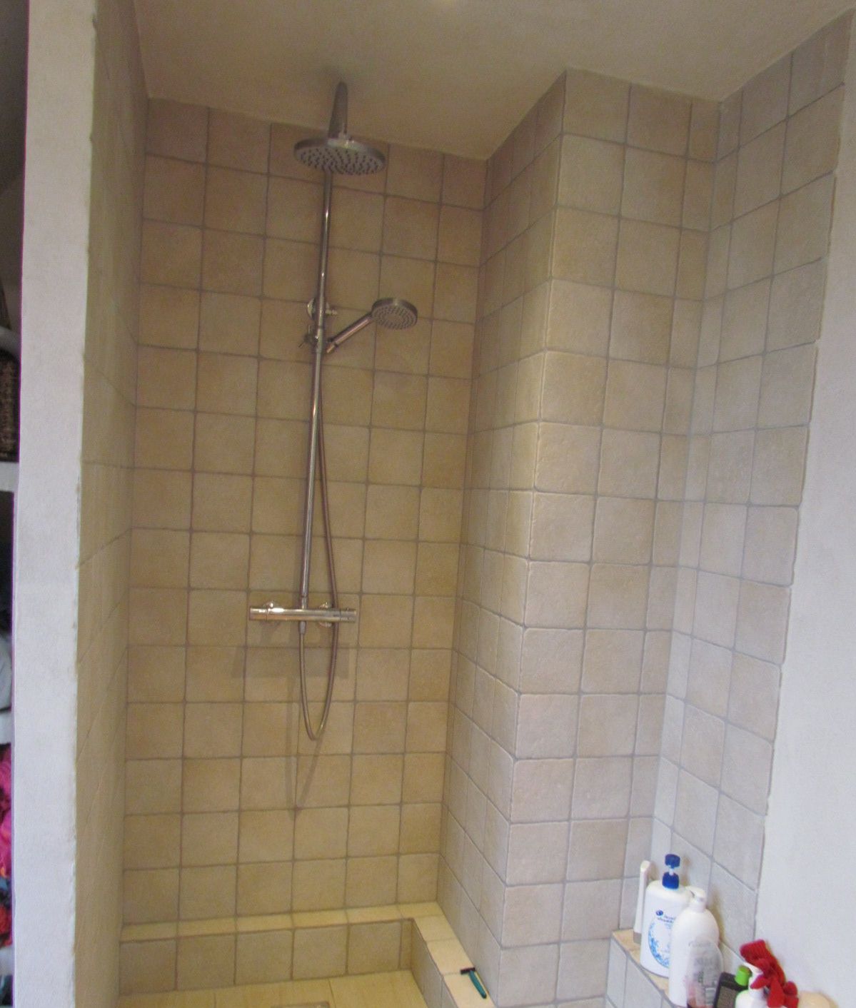 Un pequeño espacio de ducha con azulejos, un cabezal de ducha de mano y un grifo instalado en la pared.