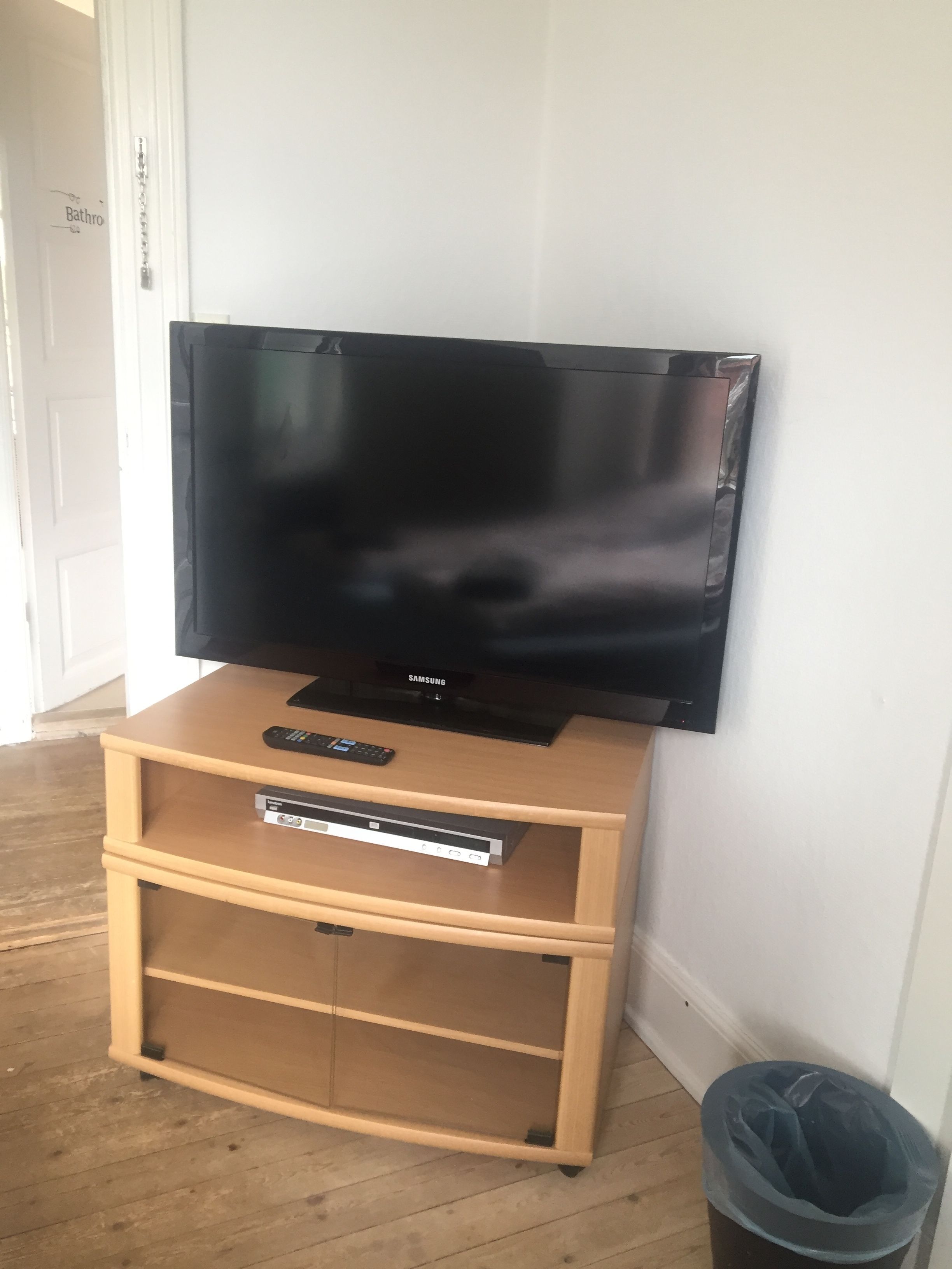 Un meuble en bois pour la télévision, avec un téléviseur à écran plat, une télécommande et un lecteur DVD.