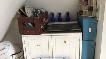 A small kitchenette with a sink, a blue refrigerator, a wooden crate with magazines, and a laundry basket.