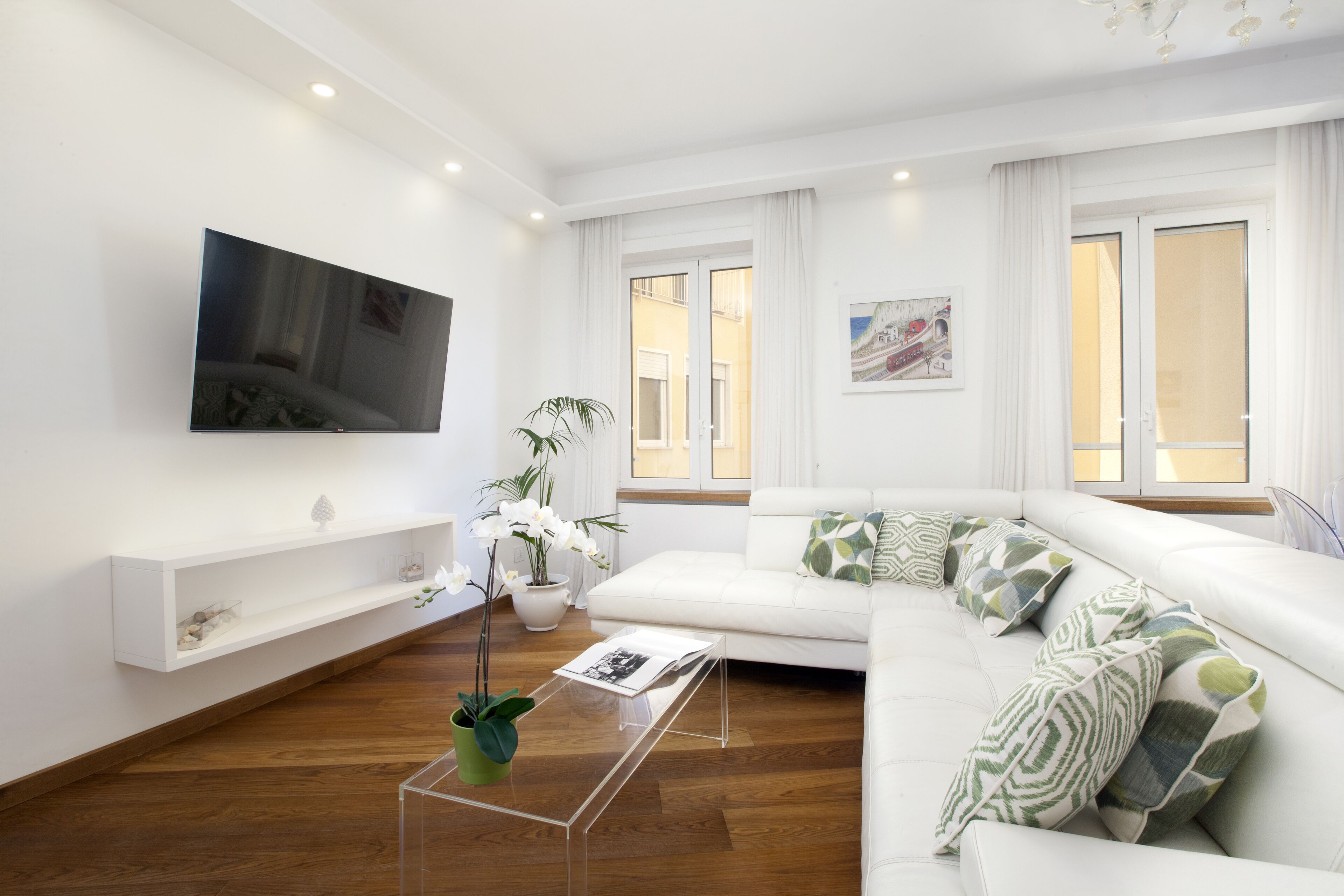 Una sala de estar moderna con un sofá blanco, un televisor de pantalla plana en la pared, una mesa de centro y una planta en maceta.