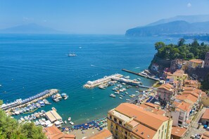 A coastal town with a marina, buildings with red-tiled roofs, and a clear view of the sea and mountains in the background. - Luxury home with sea-view (Sorrento)