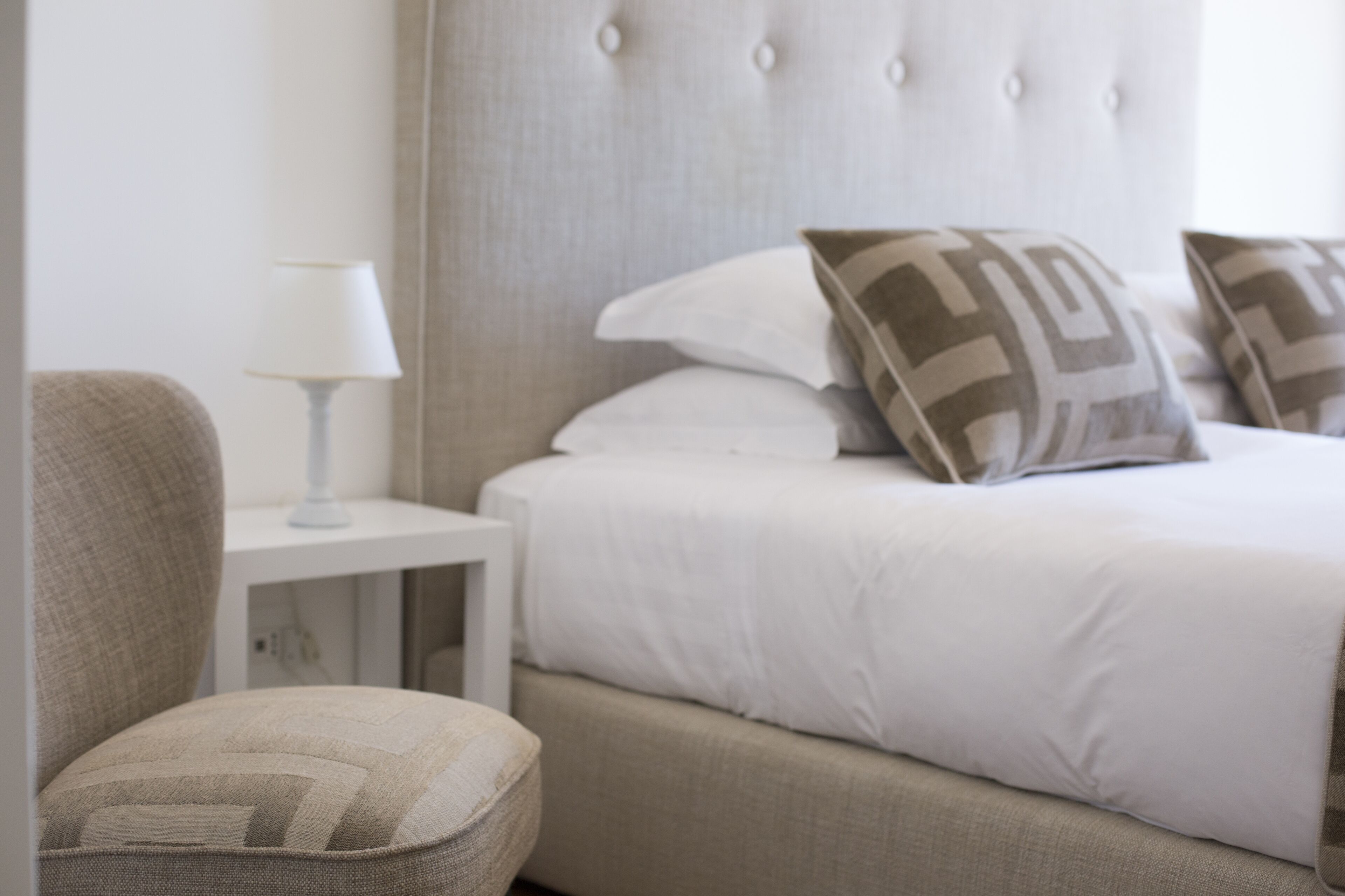 A neatly arranged bedroom with a bed, pillows, a chair, and a nightstand.