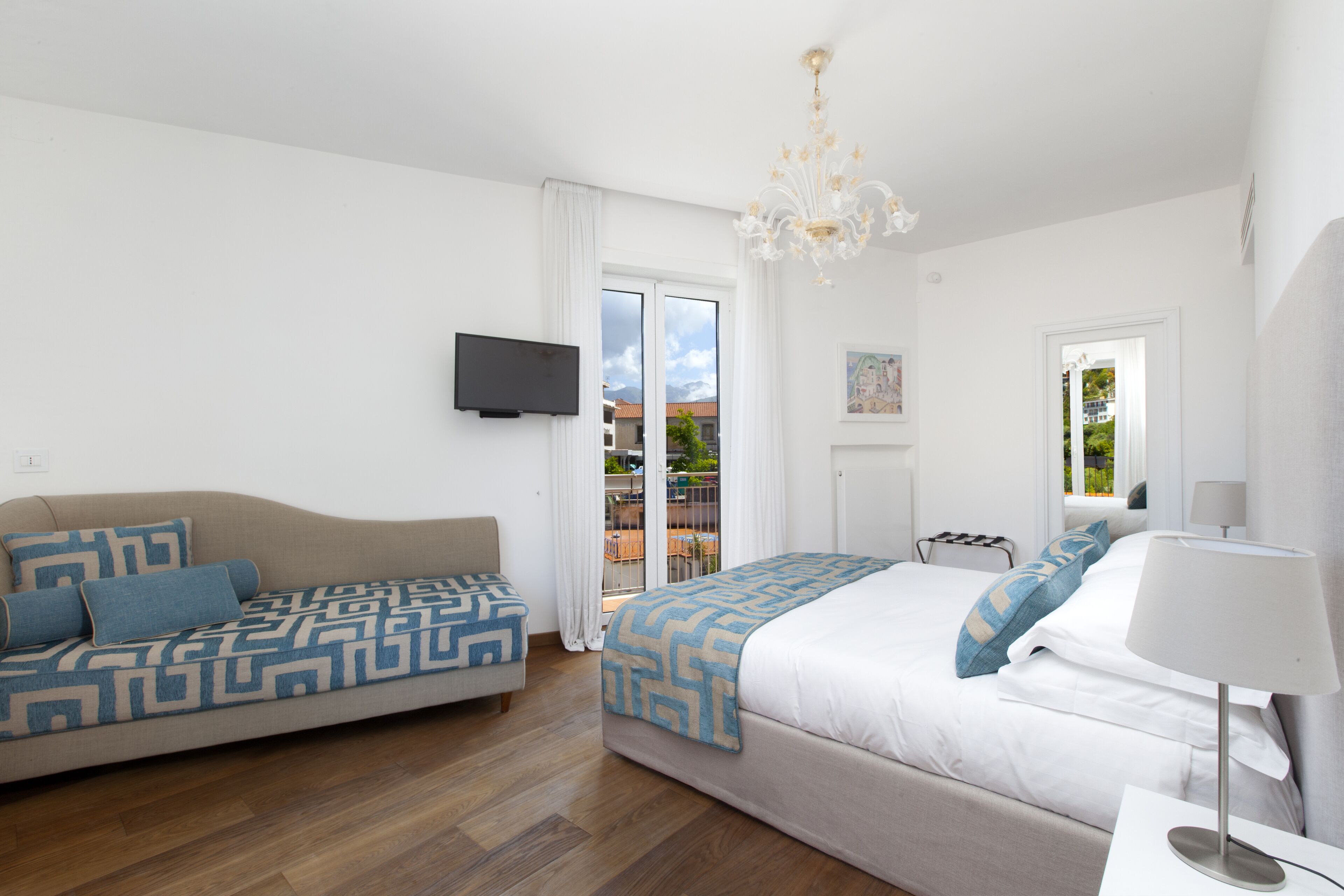 A modern hotel room with a sofa, a bed, a TV, and a balcony view.