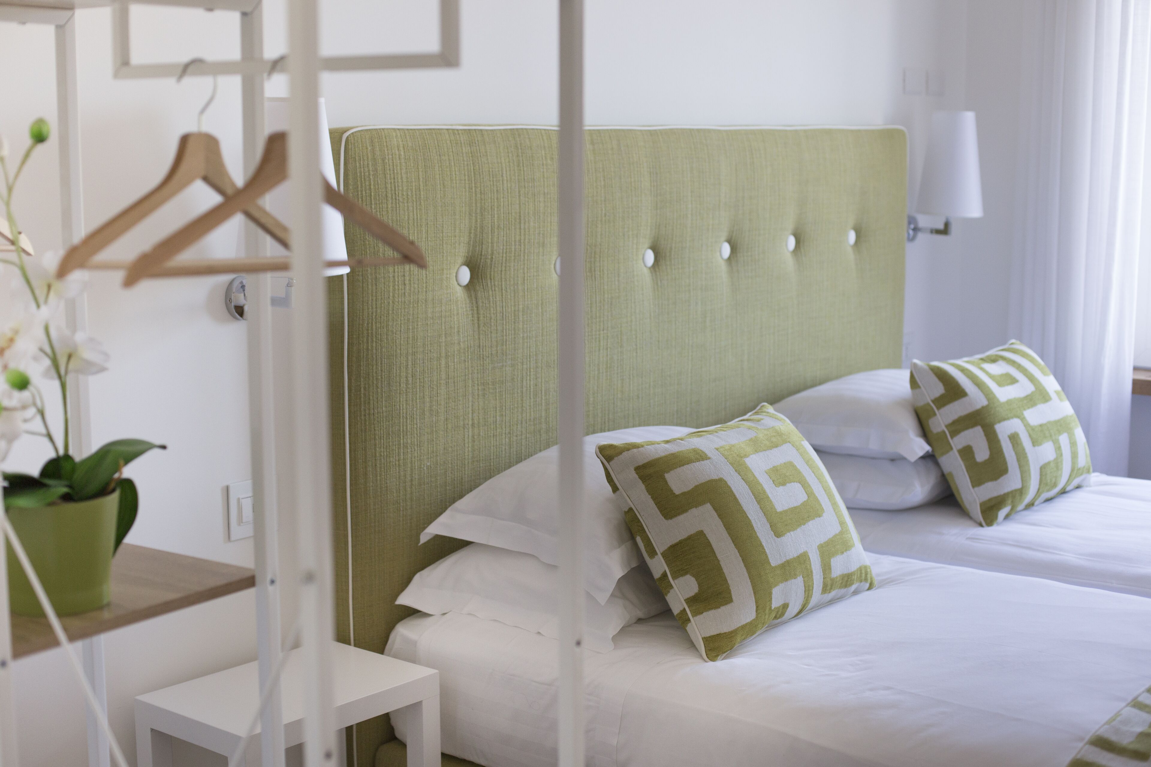 A hotel room with two beds, a hanging garment rack, a bedside table, and a potted plant.