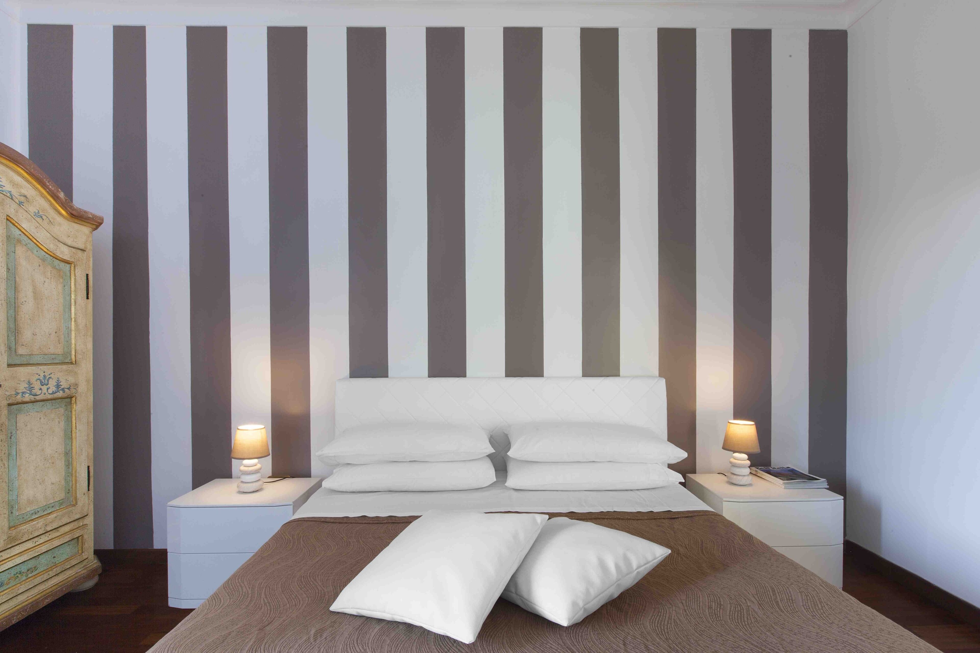 Quarto com parede listrada, cabeceira de madeira e duas mesas de cabeceira com luminárias.