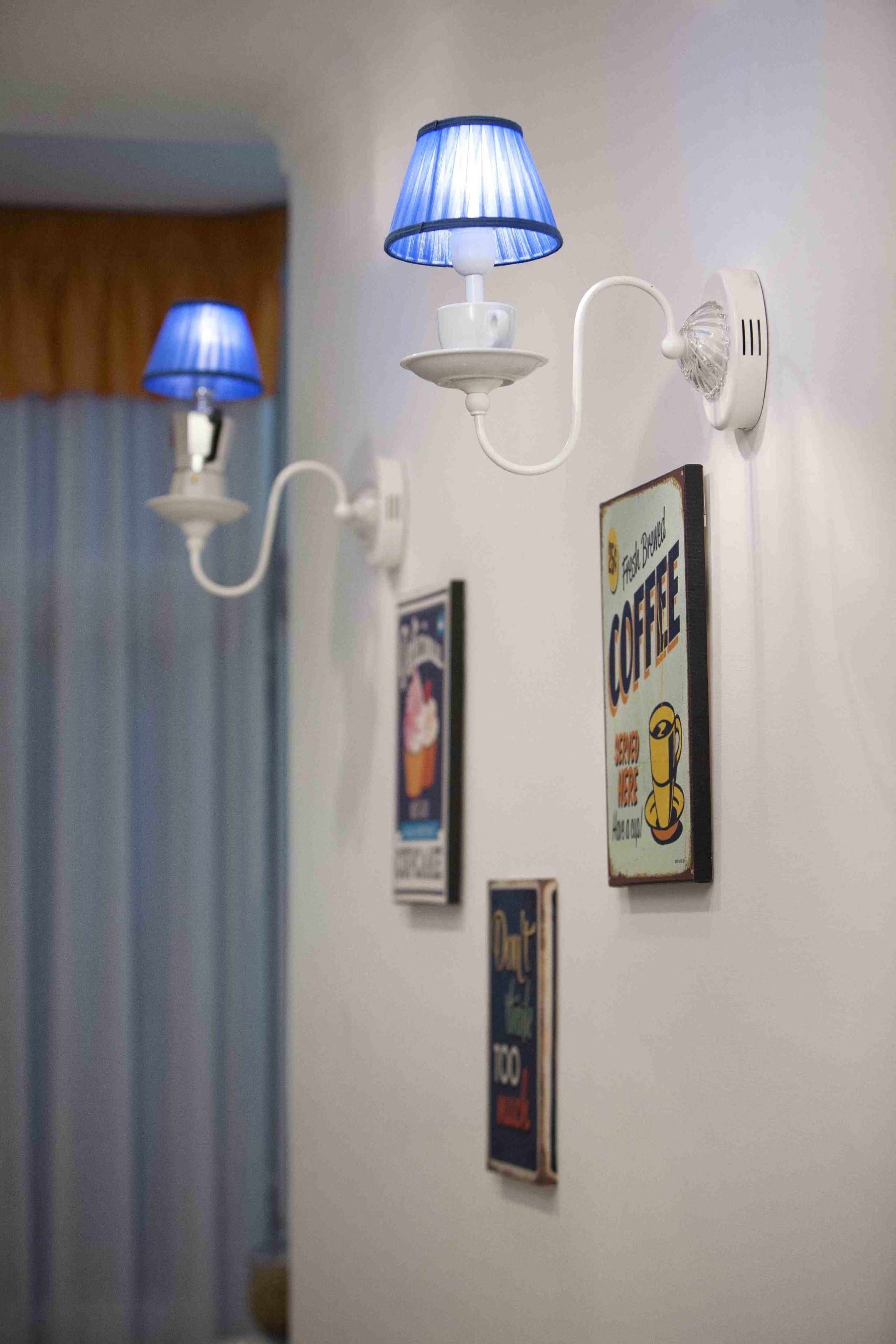 A wall-mounted lamp with a blue shade, a wall clock, and a coffee advertisement.