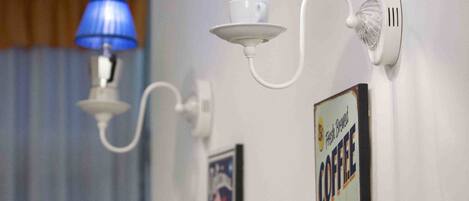 Een muurlamp met een blauwe lampenkap, een wandklok en een advertentie voor koffie.