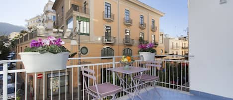 A balcony with a white railing, two purple chairs, and a table with a fruit bowl.