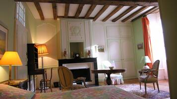 A room with a bed, a desk, a chair, and a dresser. There is a window with curtains, a lamp, and a mirror on the wall.