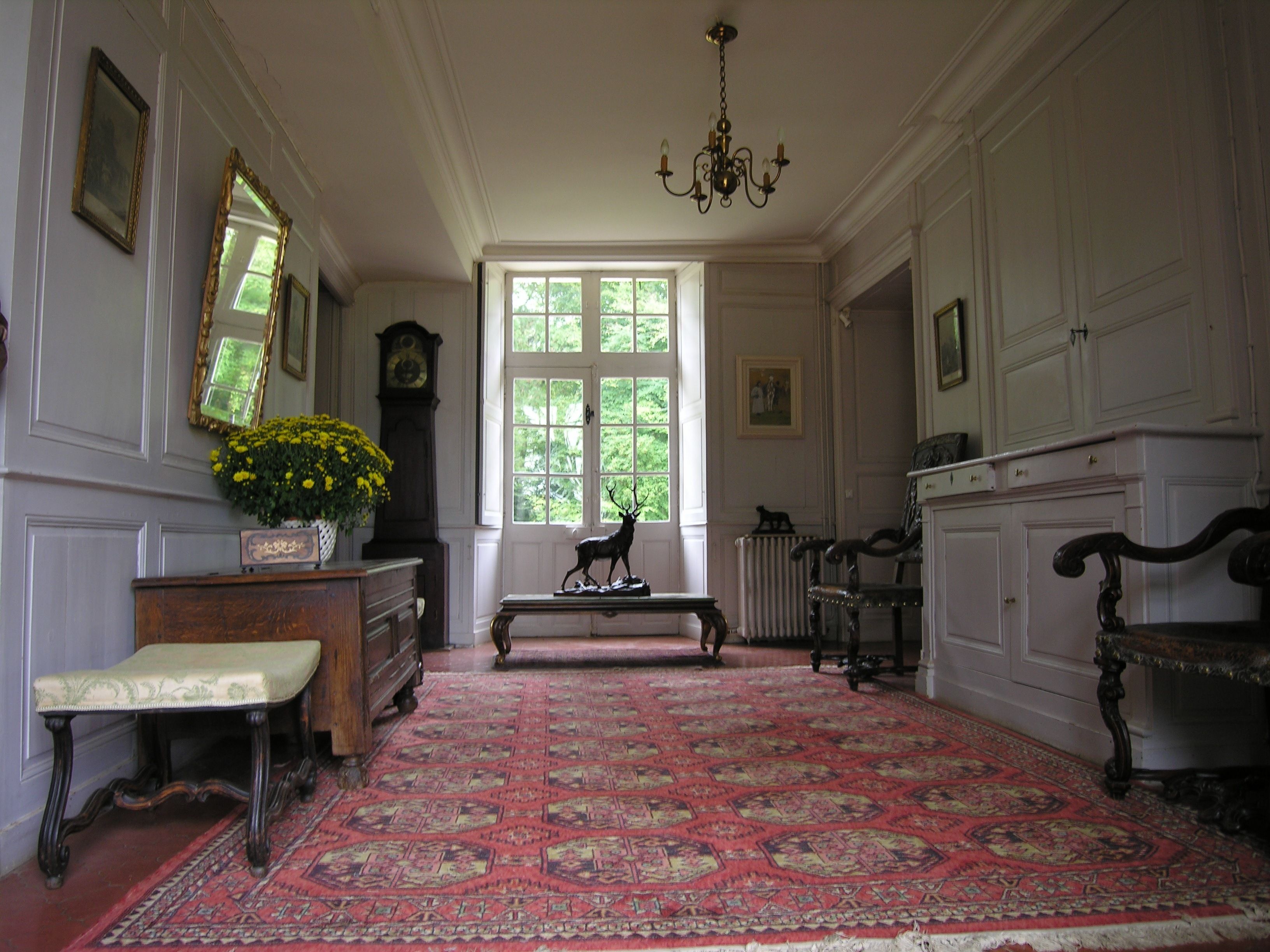 A room with a large window, a chandelier, a wooden bench, and a patterned rug.