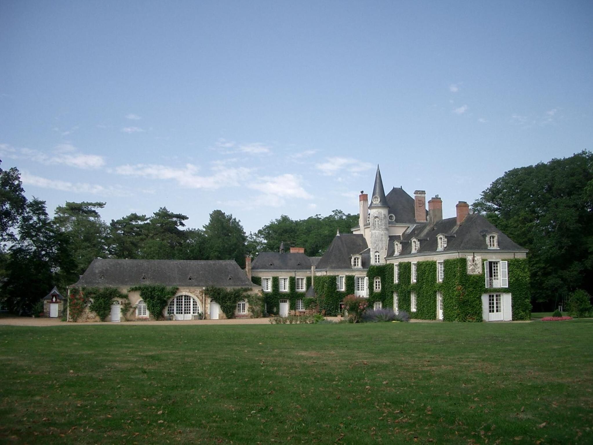 A large, historic building with a central tower and multiple wings, surrounded by a well-maintained lawn.