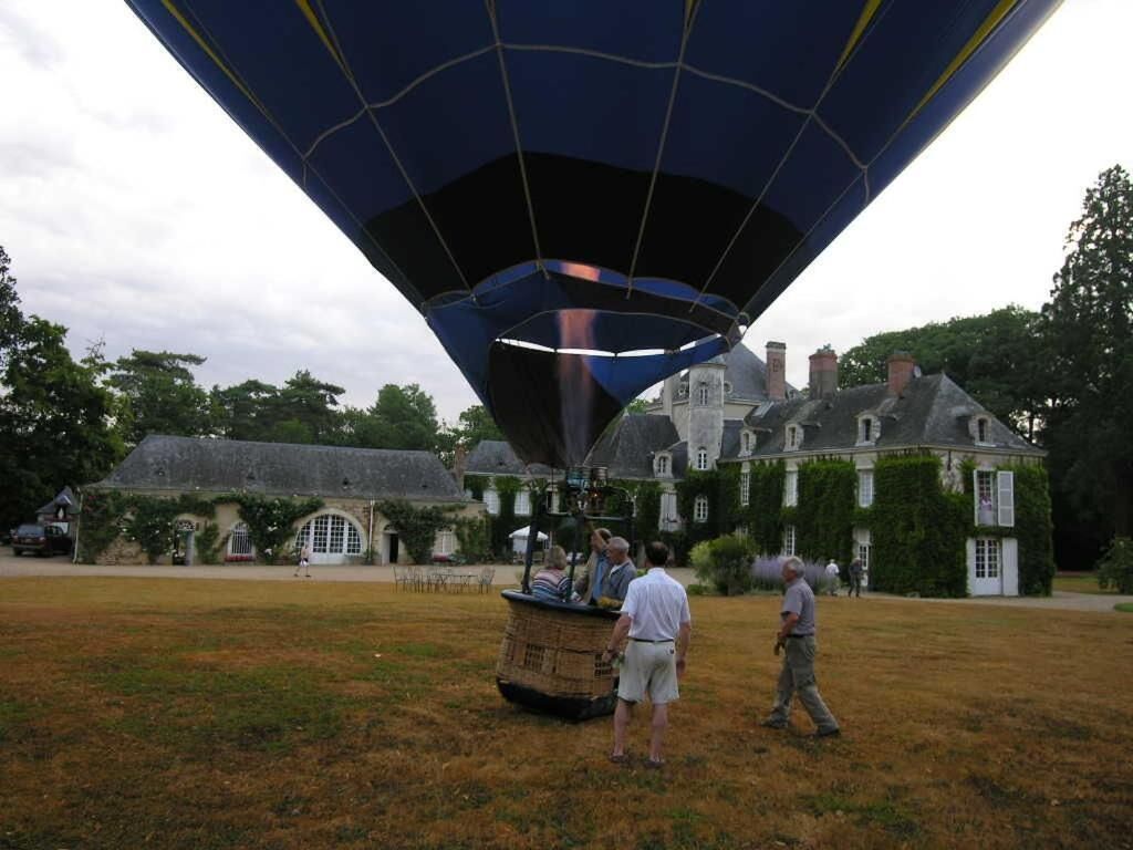 Een luchtballon met een mand, een historisch gebouw met klimopbedekte muren en een grasveld.