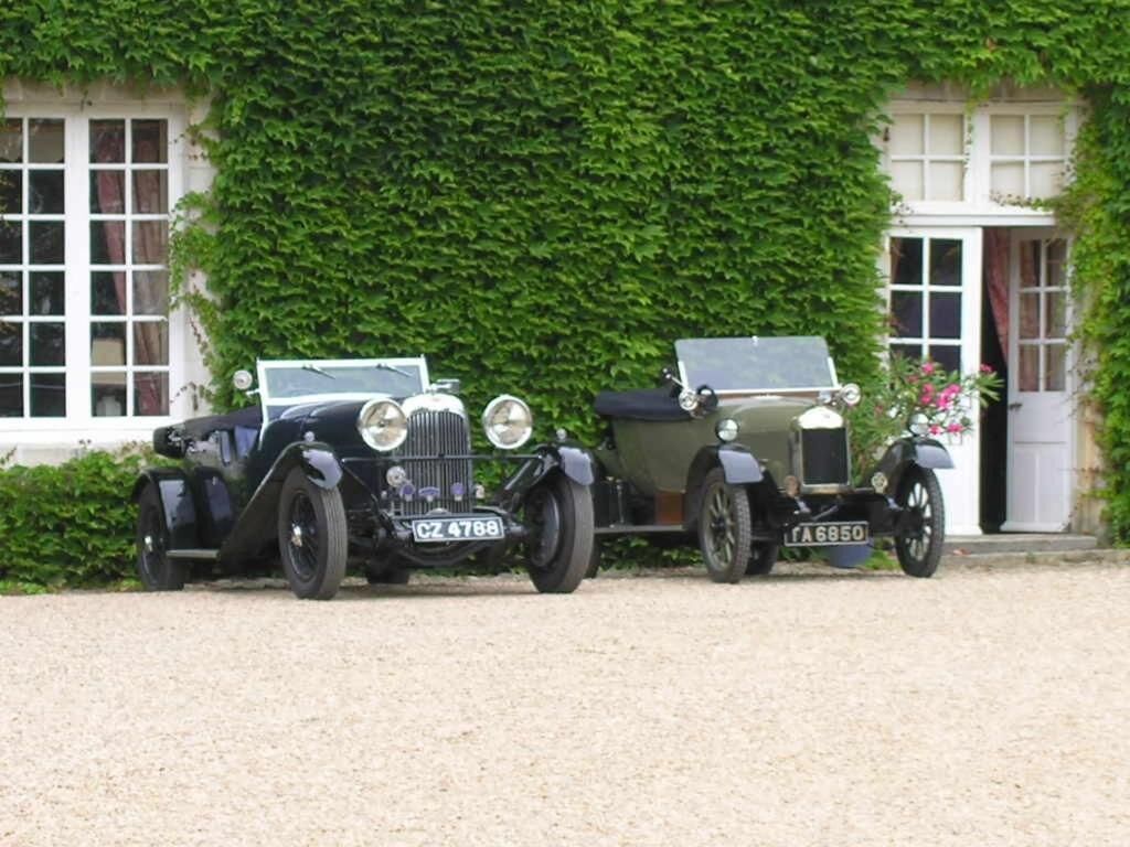 Two vintage cars parked in front of a building with a green ivy-covered wall.
