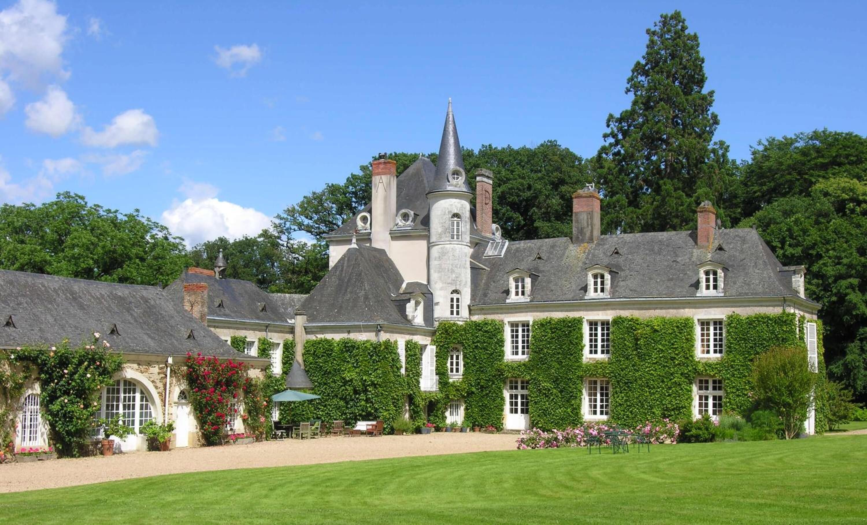 A large, historic building with multiple towers and a well-maintained garden.