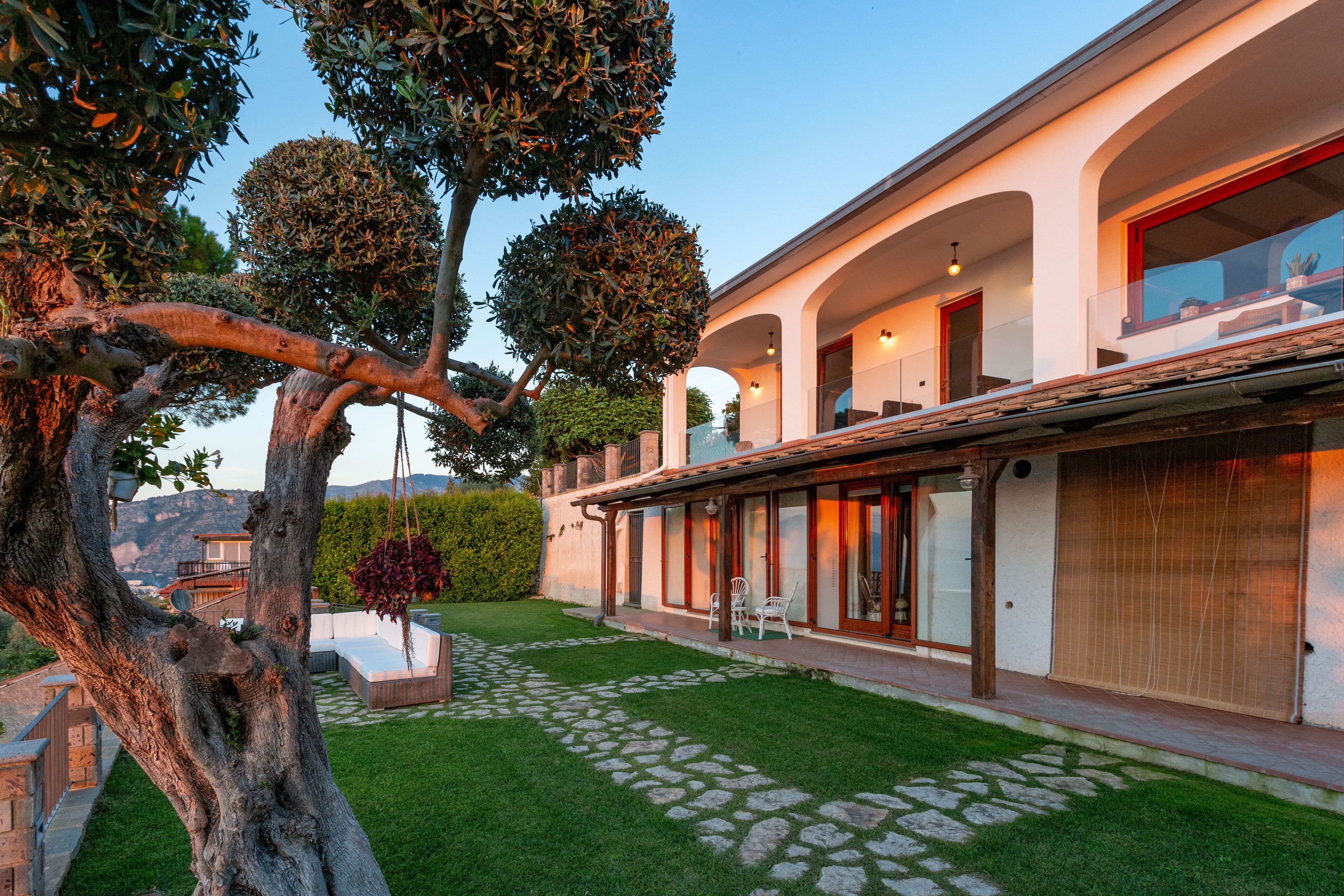 Una casa moderna con un camino de piedra, un césped cuidado y un árbol grande.