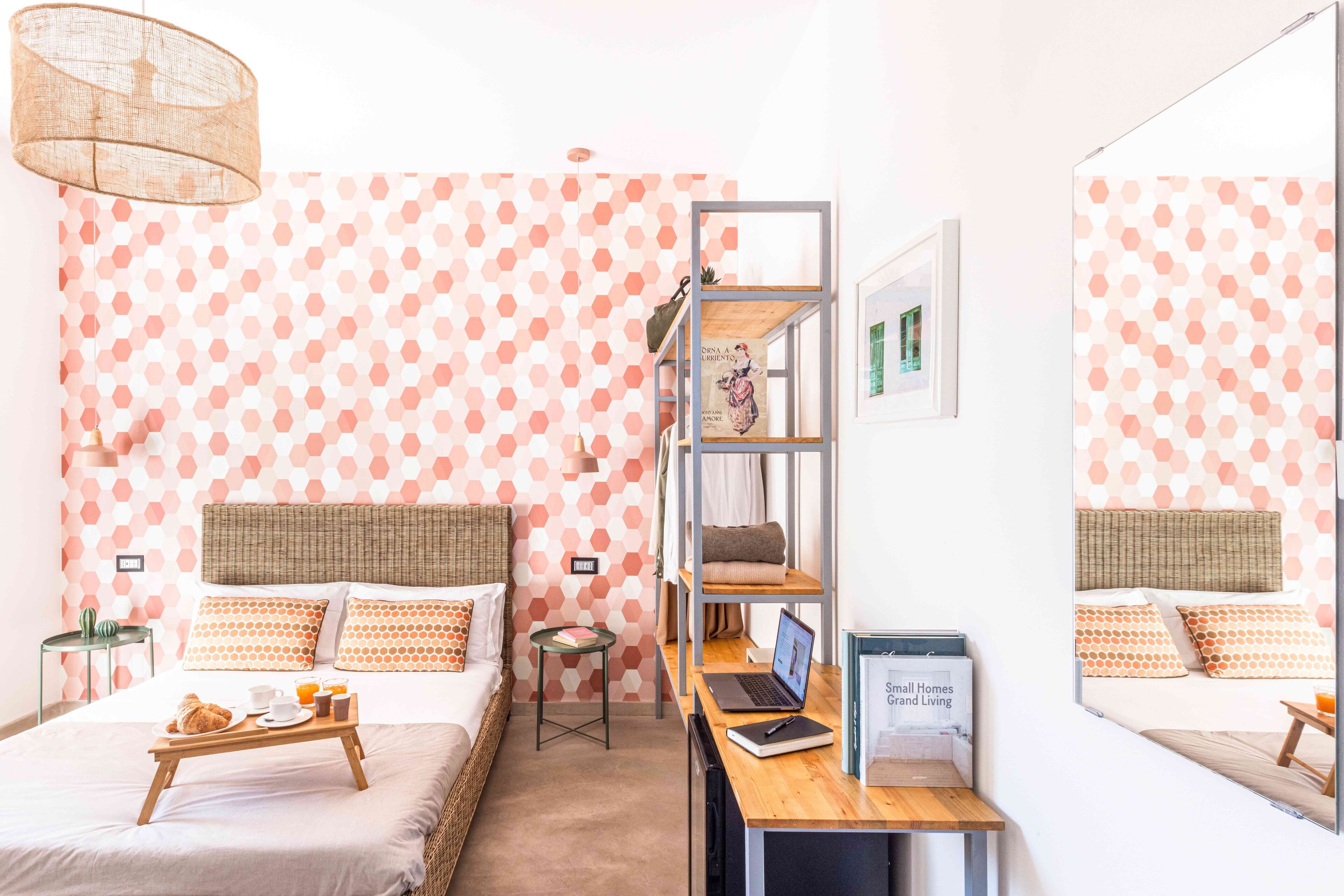 A bedroom with a bed, a desk with a laptop, a small table with breakfast, and a bookshelf.