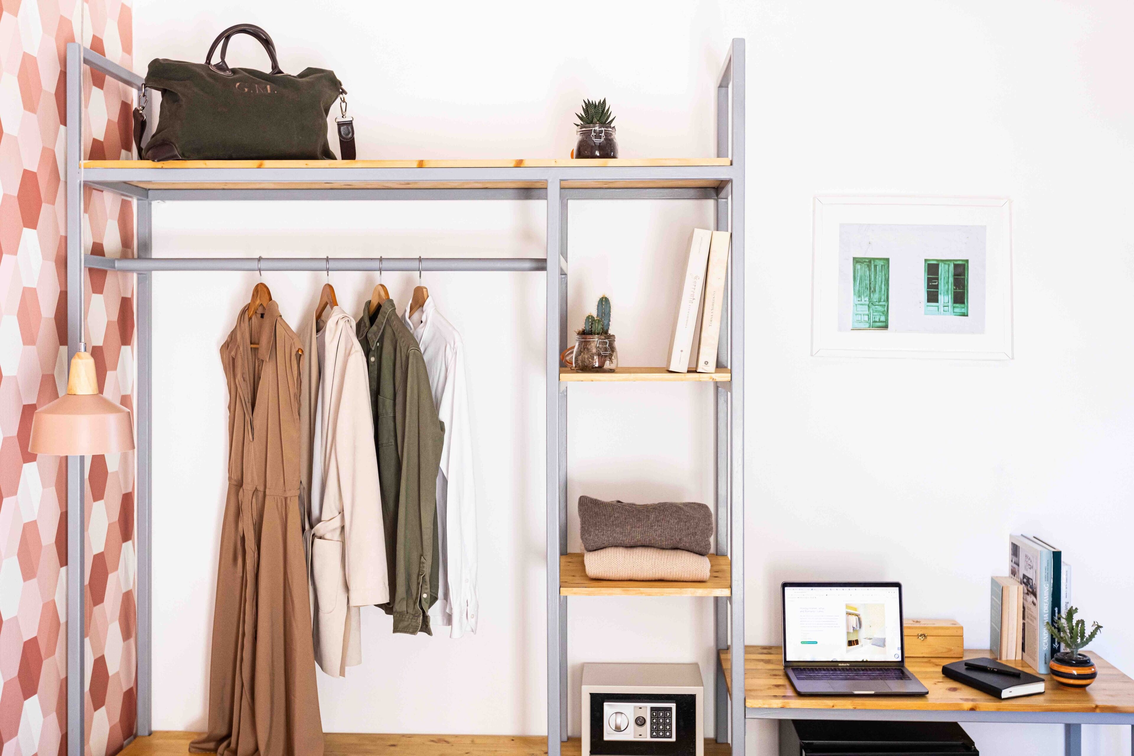 A room with a metal shelving unit holding clothes, a laptop, and a small plant.
