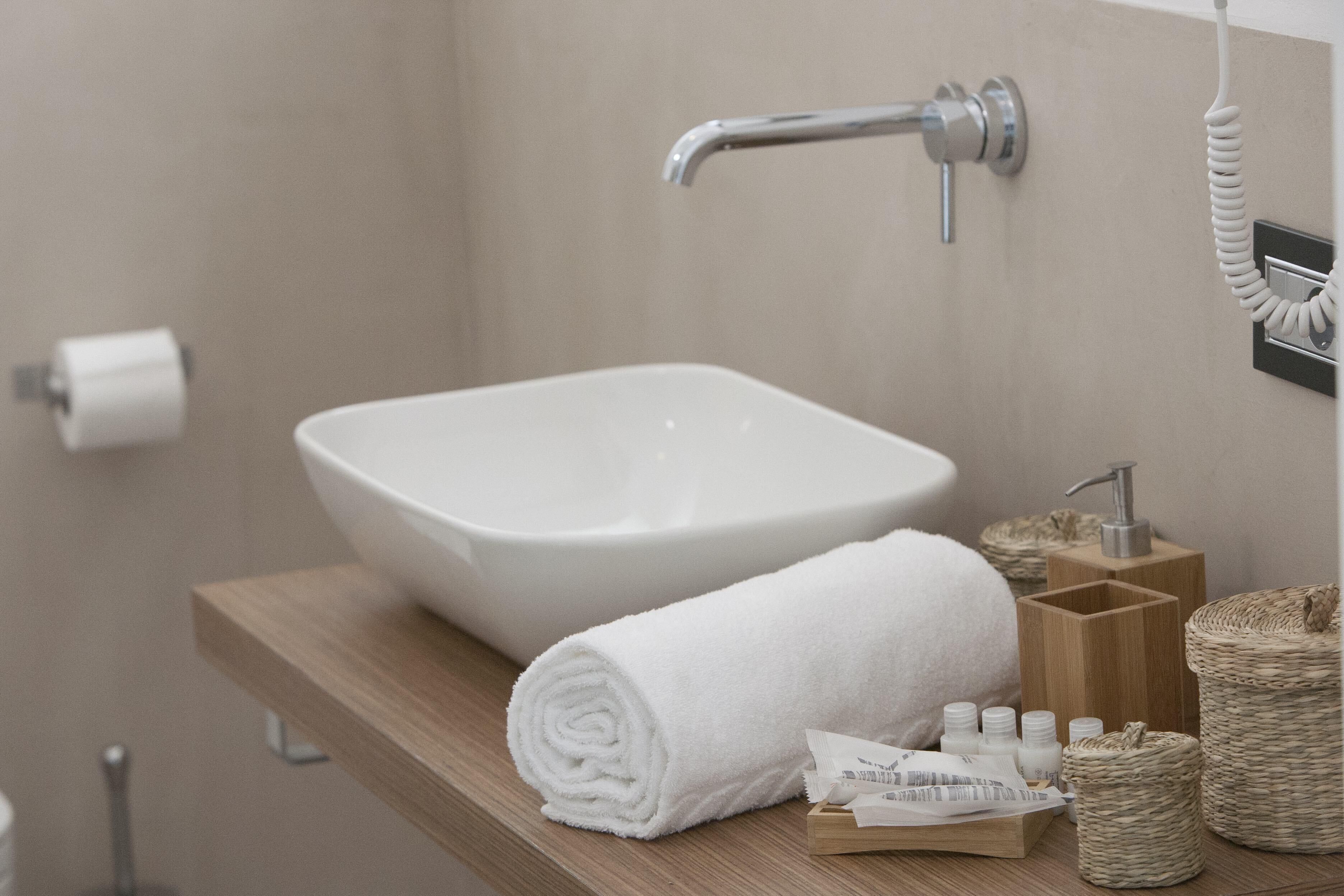 Une salle de bain avec un lavabo blanc, une serviette, des articles de toilette et un meuble-lavabo en bois.