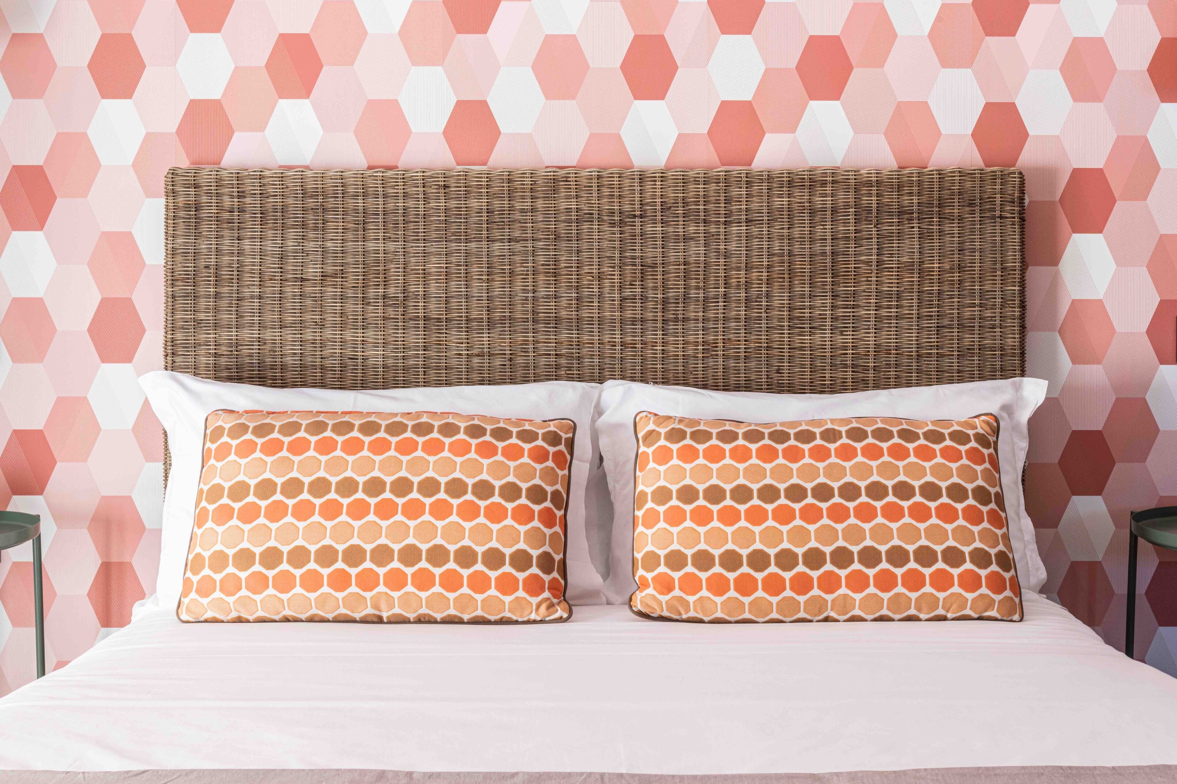 A bed with a woven headboard, two matching pillows, and a patterned wall.