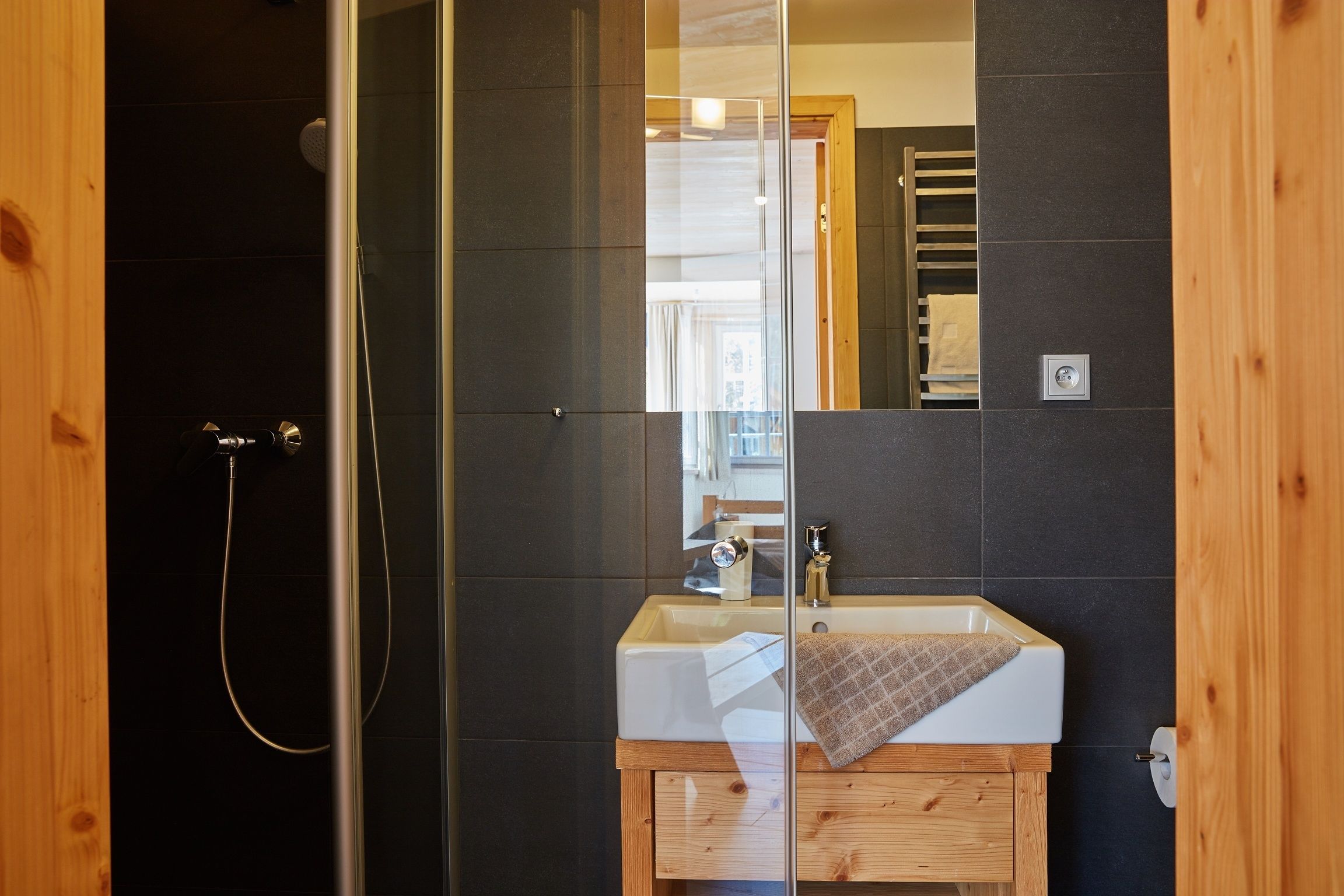 Un baño con cabina de ducha de vidrio, un lavamanos blanco y un mueble de tocador de madera.