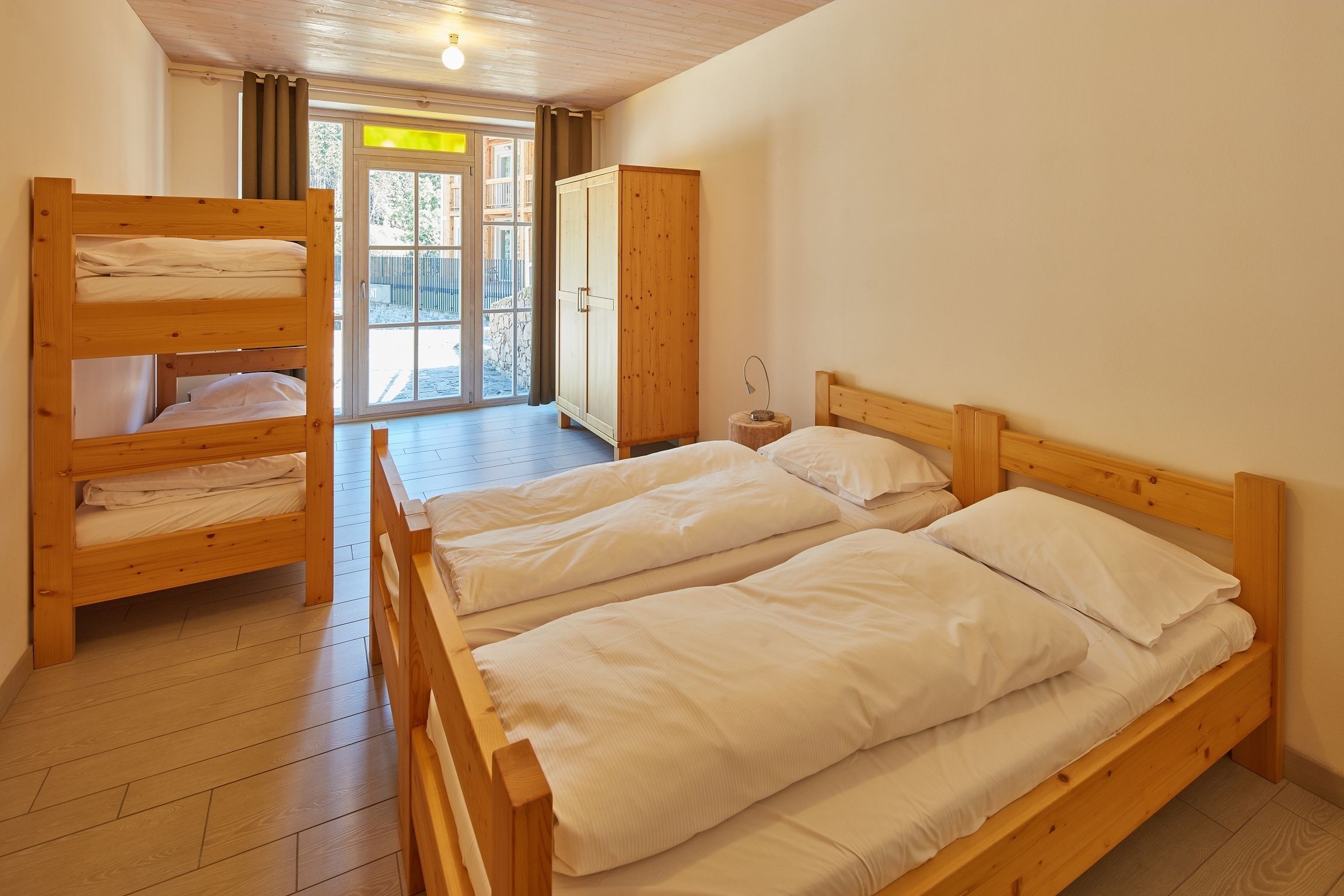 Una habitación con dos camas literas de madera, un armario de madera y una pequeña mesa.