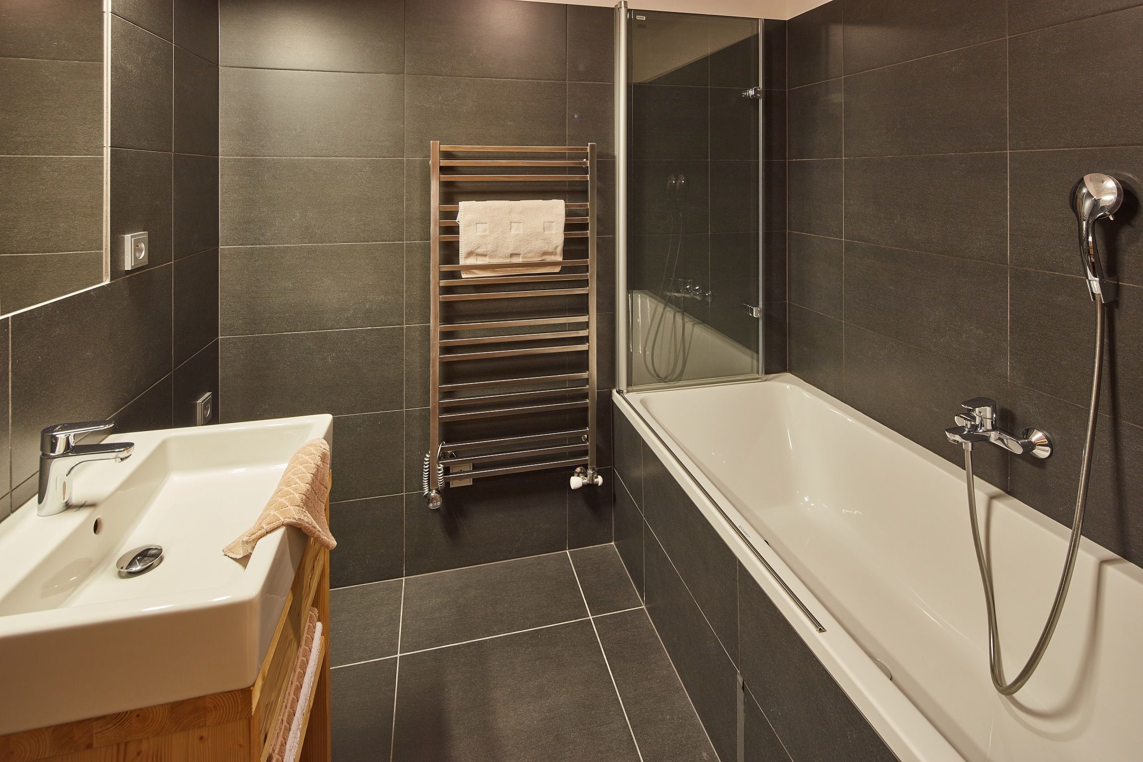 A modern bathroom with a white sink, a glass-enclosed shower, and a towel rack.