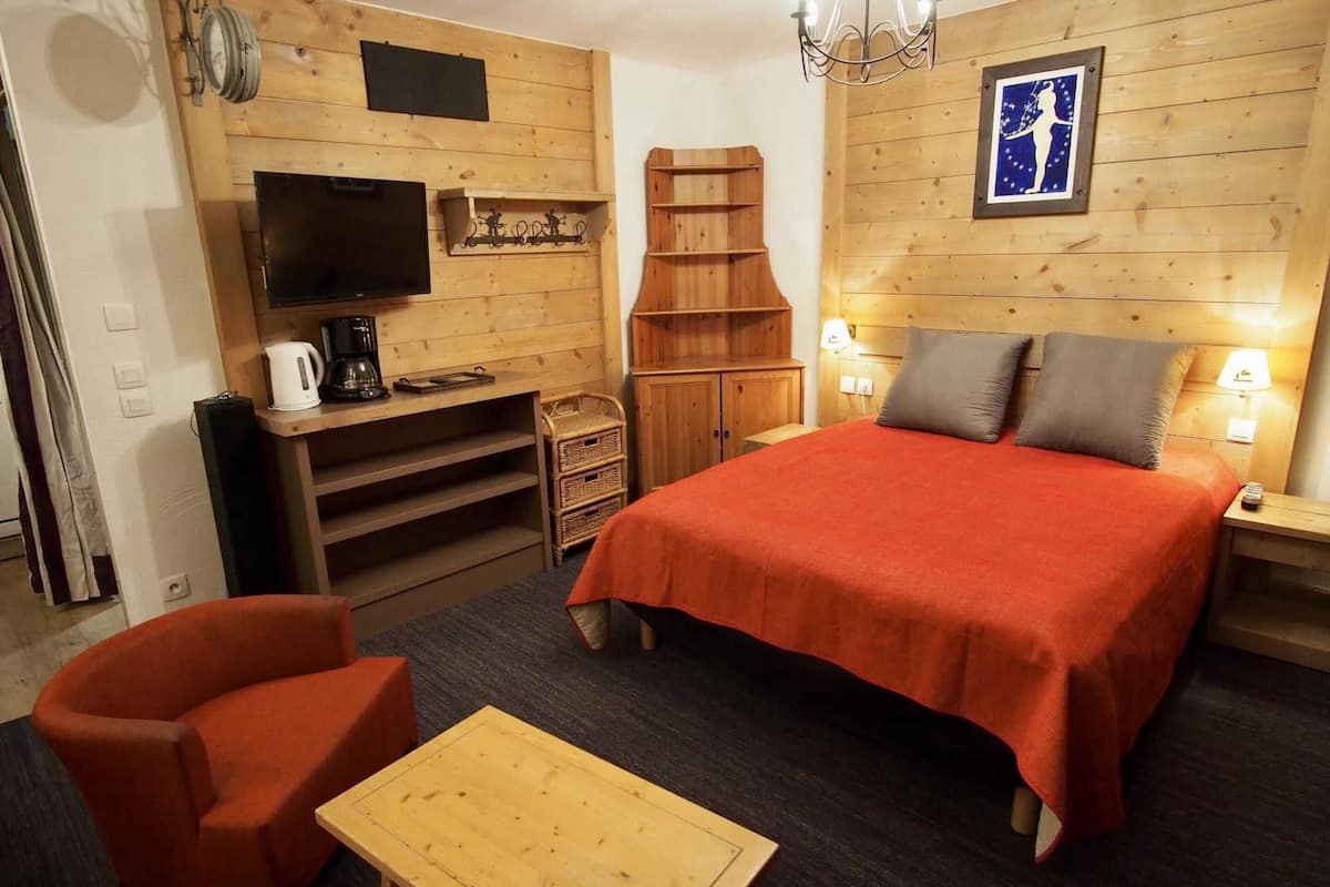 A cozy room with a bed, a TV, a coffee maker, and a TV shelf.
