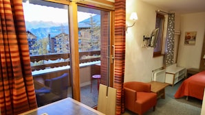 A hotel room with a balcony, a small table, two chairs, a bed with a red cover, and a view of mountains through the window. - RisoulSki Antarès (Risoul)