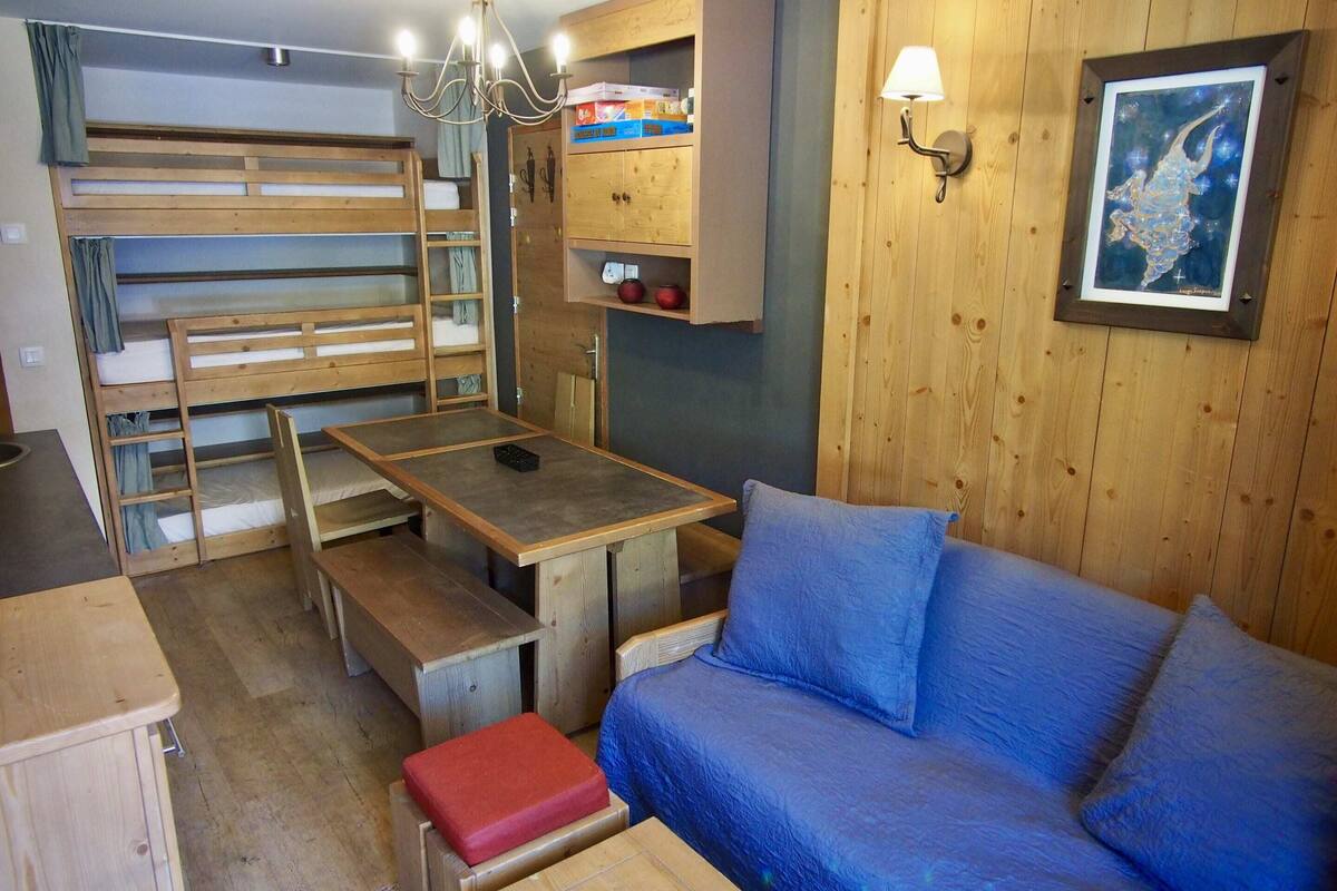 A compact room with bunk beds, a wooden table, a sofa, and a wall-mounted cabinet.