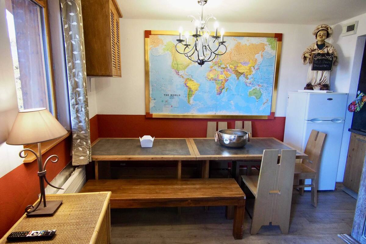 A dining area with a wooden table, chairs, a chandelier, a map on the wall, and a refrigerator.