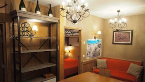 A cozy room with a wooden table, a red sofa, and a chandelier. There are shelves with bottles and a lamp. - RisoulSki Antarès (Risoul)