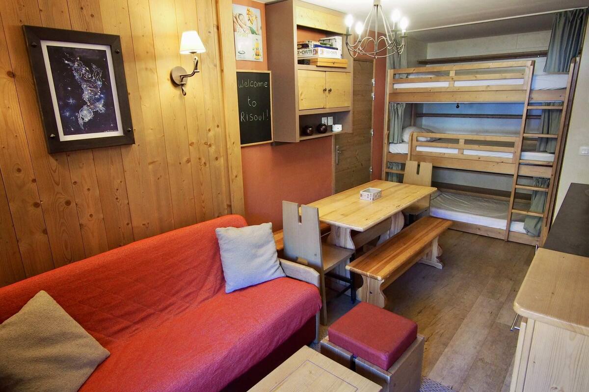 A cozy room with a bunk bed, a wooden table, a red sofa, and a chalkboard with a welcome message.