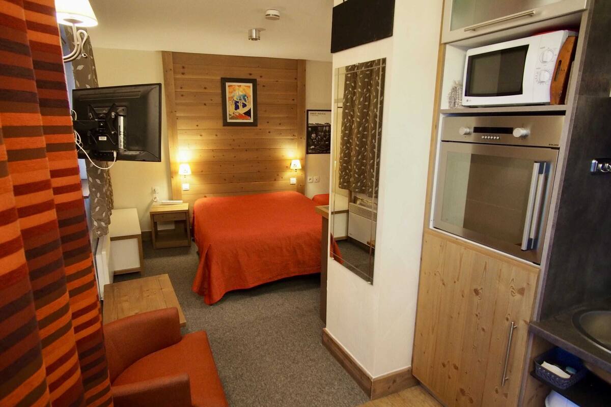 A compact hotel room with a bed, a TV, a microwave, and a small kitchenette.
