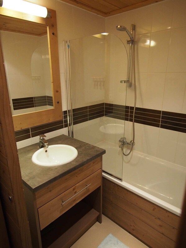 Un baño con tocador de madera, lavamanos, espejo, ducha y bañera.