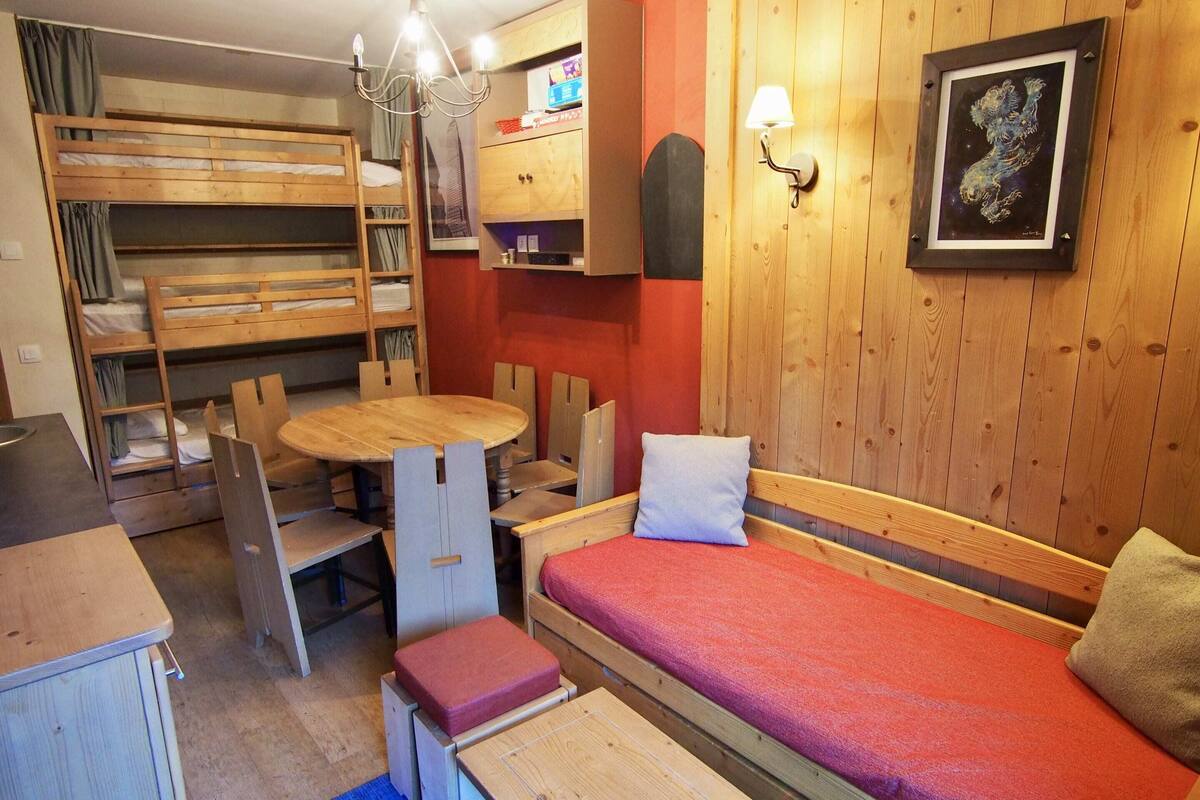 A compact room with bunk beds, a small dining table, and a single bed with a red blanket.