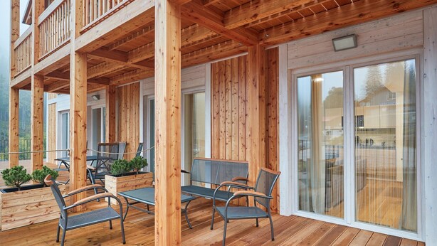 A wooden deck with outdoor furniture, including chairs and a table, and a glass door leading to a covered area.