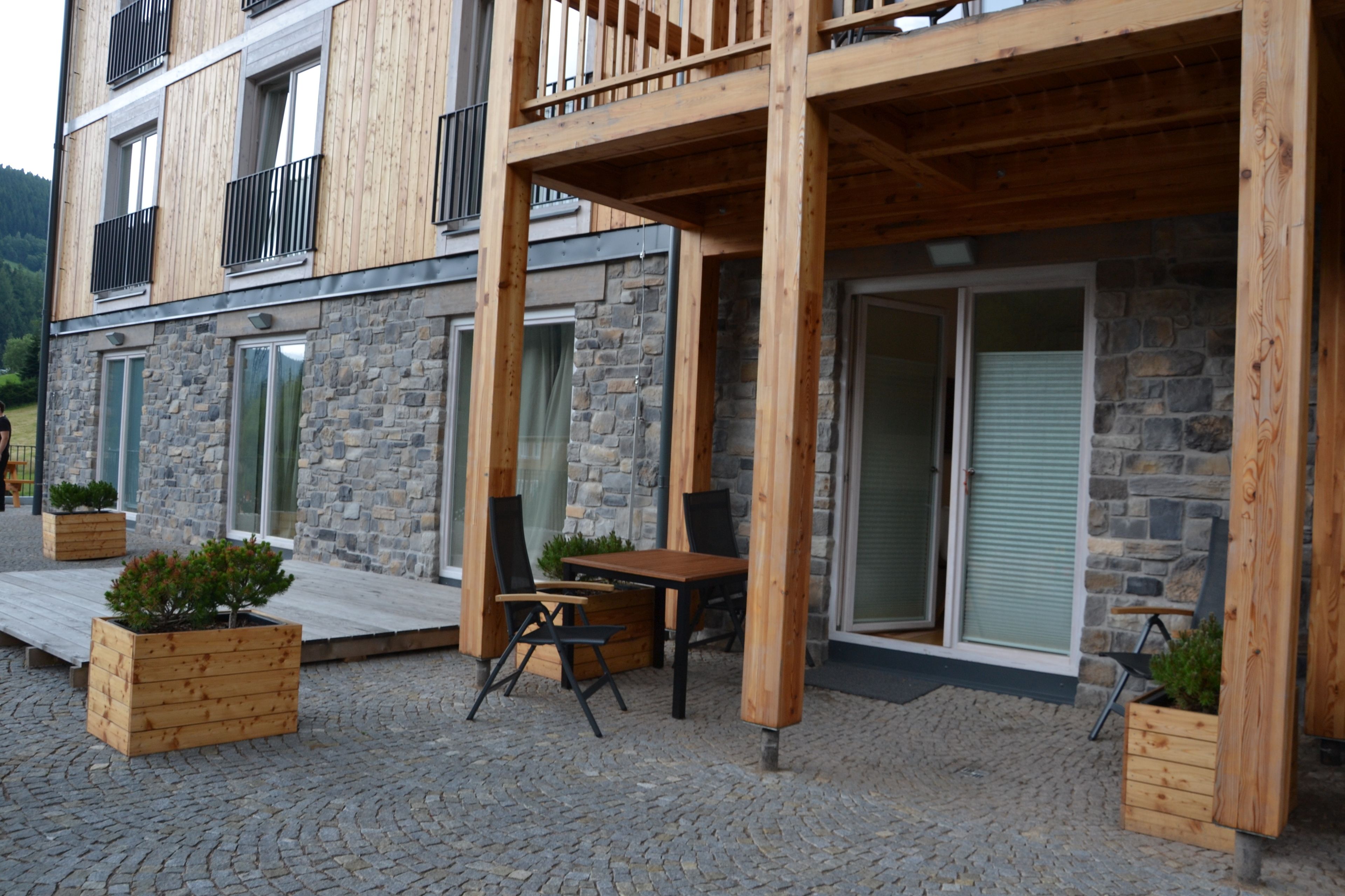 A modern building with a stone facade, wooden balcony, and outdoor seating area.