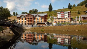 A lakeside hotel with a reflection in the water, a bridge, and a hilly landscape.