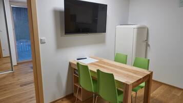 Ein Zimmer mit Holztisch, grünen Stühlen, einem Flachbildfernseher und einem weißen Schrank.
