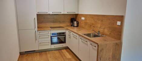 Una cocina compacta con armarios blancos, encimera de madera, horno integrado y cafetera.