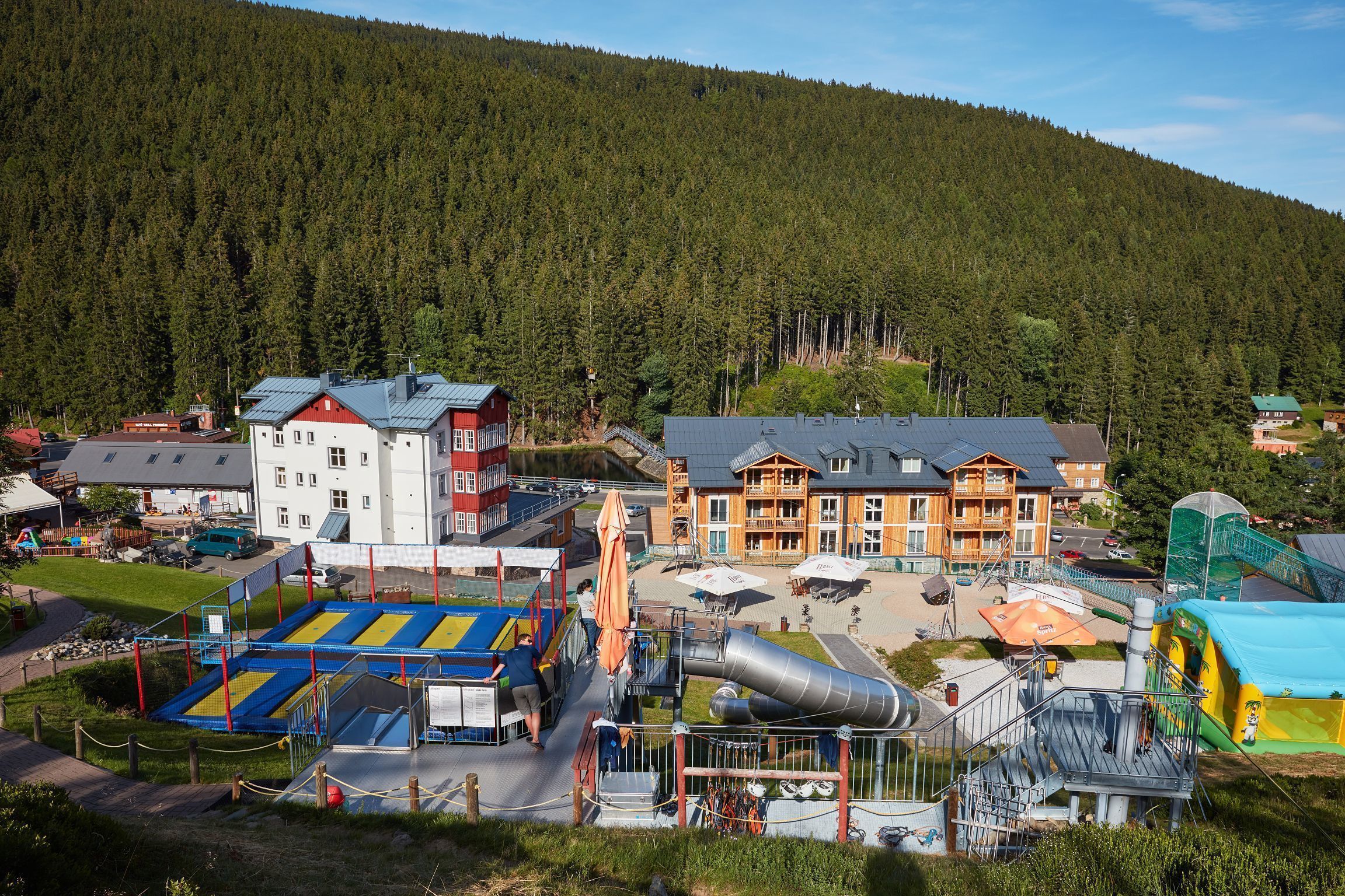 Un resort con un parque infantil, un edificio de techo rojo y el paisaje de una montaña al fondo.