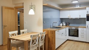 A modern kitchen with white cabinets, a wooden dining table, and a built-in oven.
