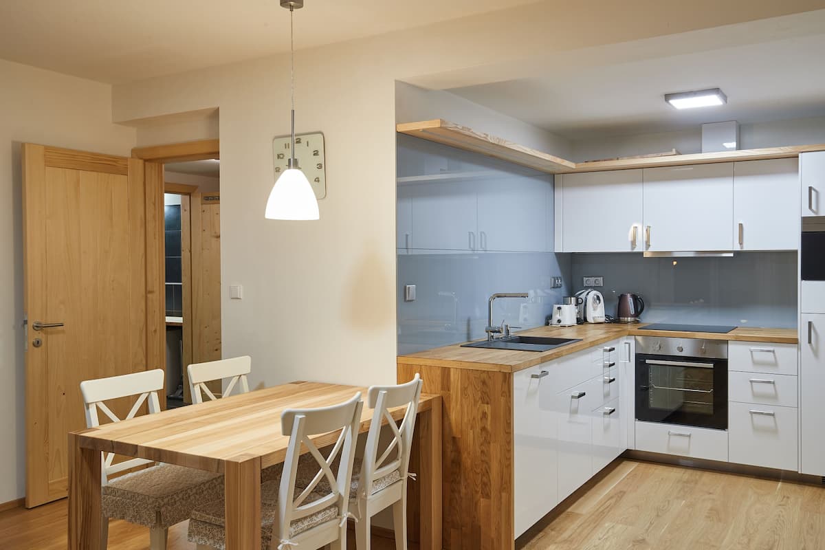 A modern kitchen with white cabinets, a wooden dining table, and a built-in oven.