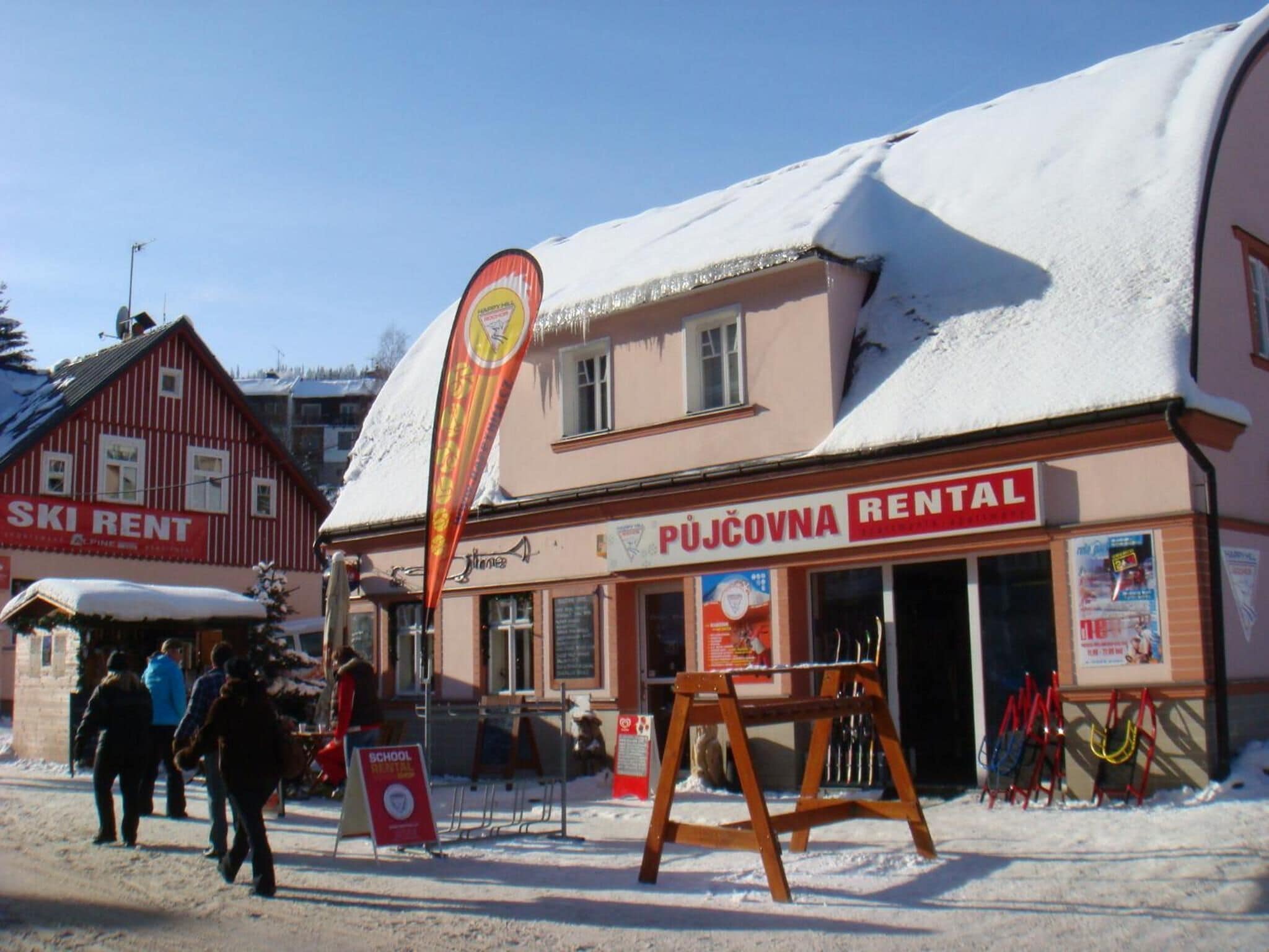 A building with a sign for 'PUJČOVNA RENTAL' and a 'Ski Rent' sign in the background.