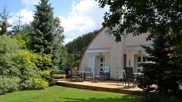 A house with a covered patio area, a small garden, and a variety of trees and shrubs. - Apartments Holiday Pec (Pec pod Snezkou)