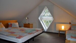 A bedroom with a sloped ceiling, a bed with a colorful quilt, a bedside table with a lamp, and a window with blinds. - Apartments Holiday Pec (Pec pod Snezkou)