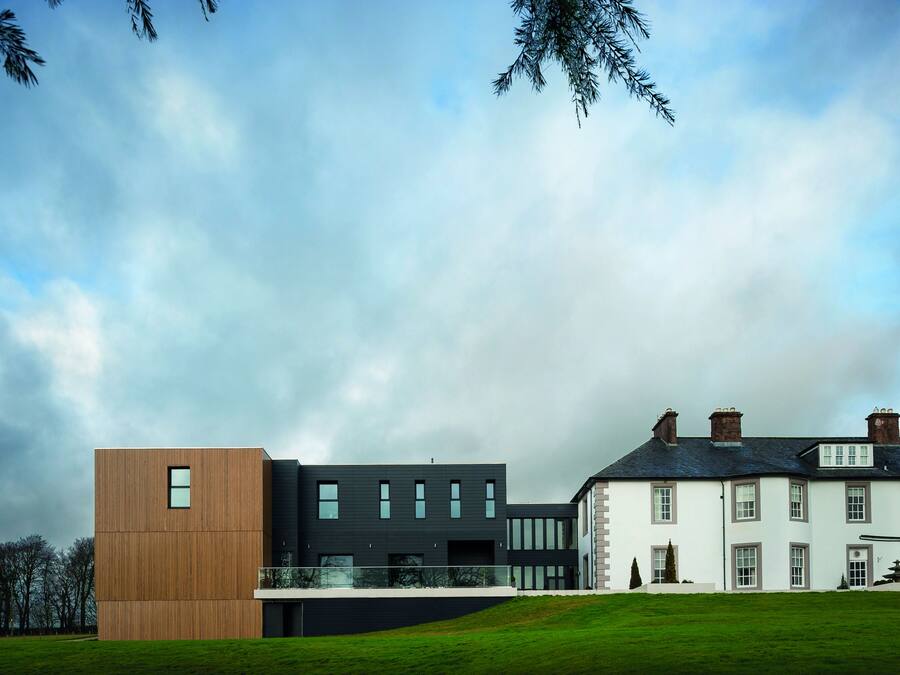 A modern building with a mix of wooden and dark-colored panels, large windows, and a well-maintained lawn.